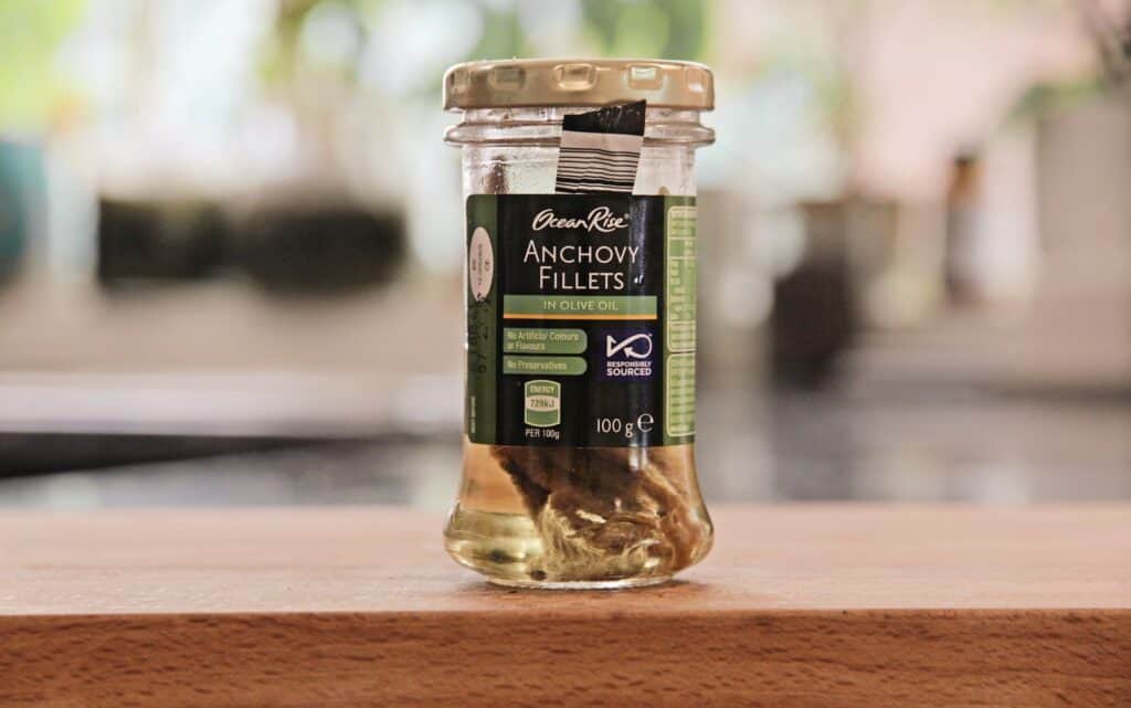 a jar of Anchovy sitting on top of a wooden table