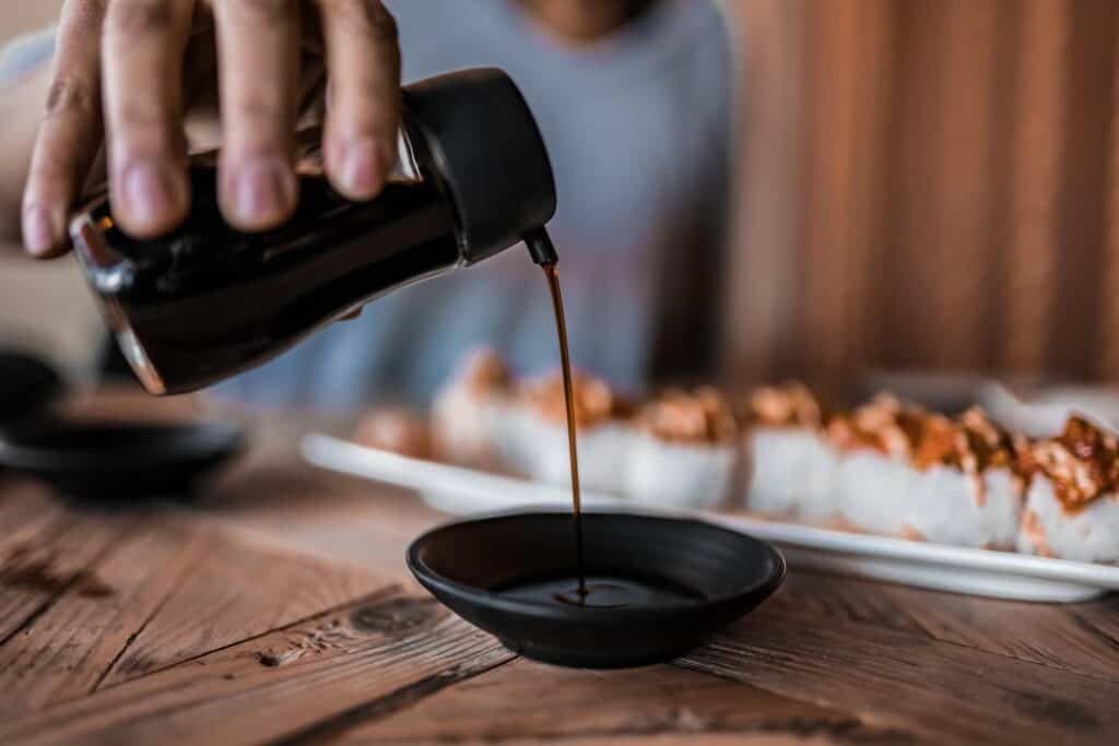 person pouring soy sauce on black ceramic mug